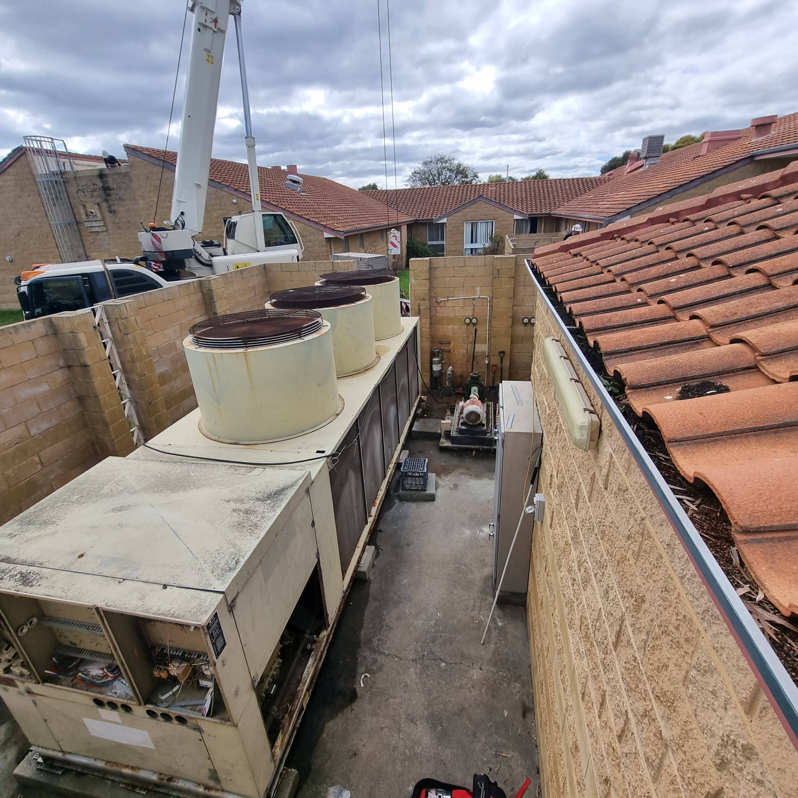 A large power conduit for an industrial air conditioning system next to a building with a red tiled roof