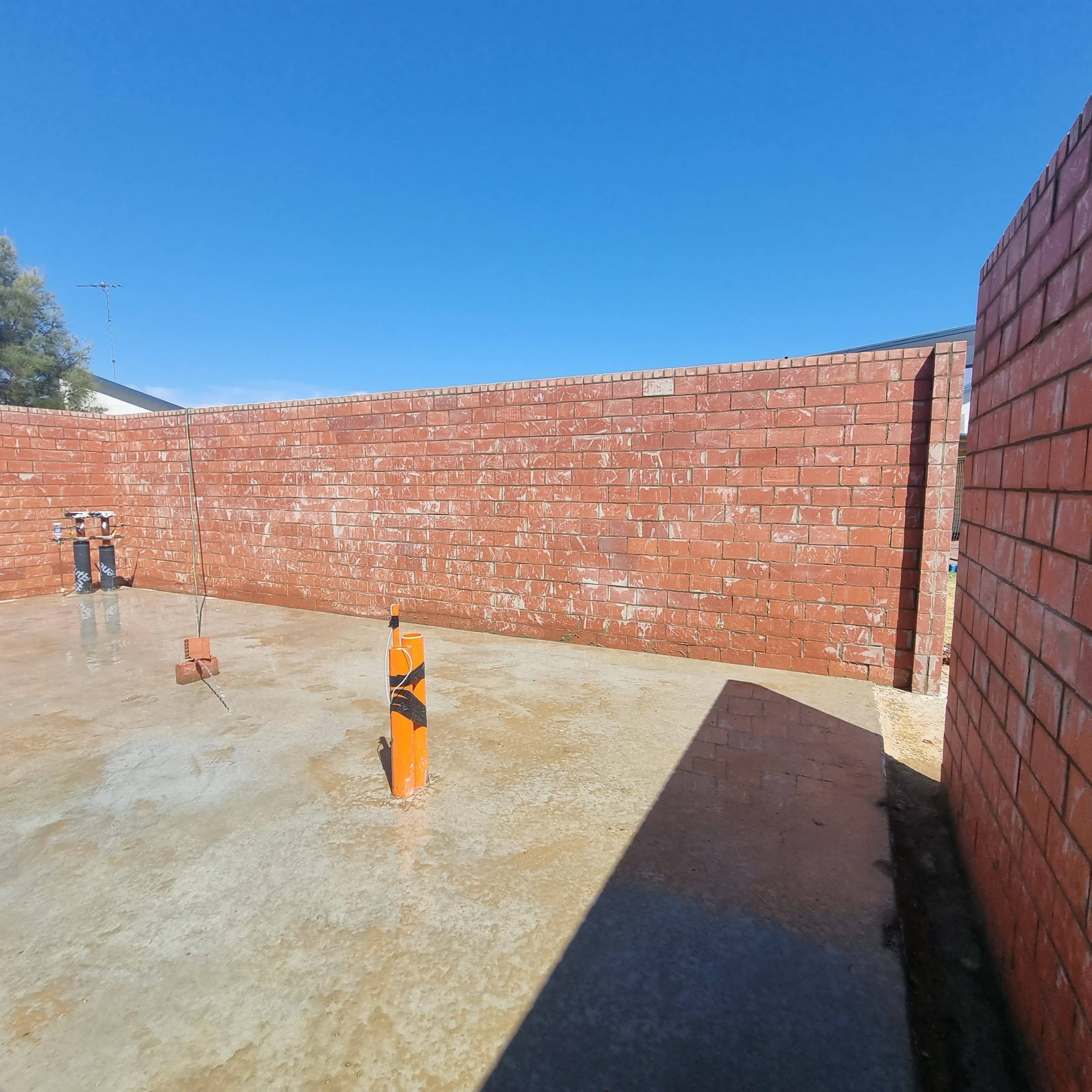 Freshly laid concrete in an outdoor area surrounded by a red brick wall