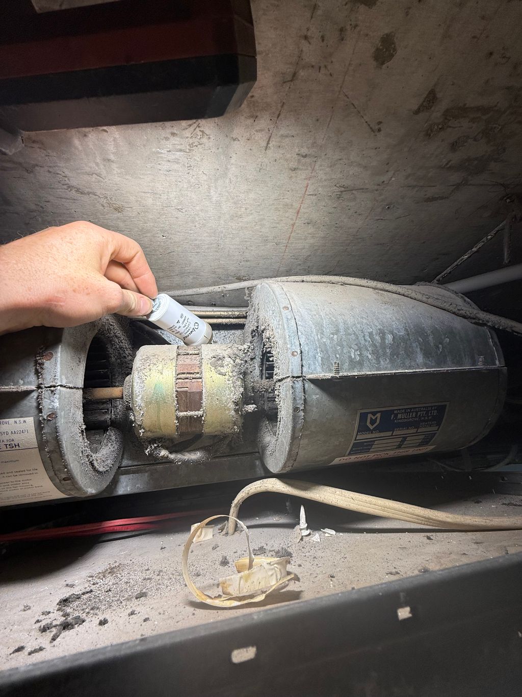Technician applying lubricant to a fan motor inside a dusty air handling unit.