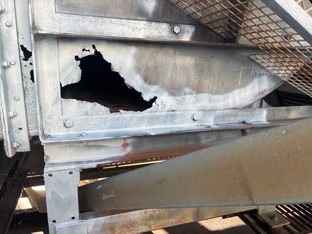 Severely corroded cooling tower panel with a large rusted hole.