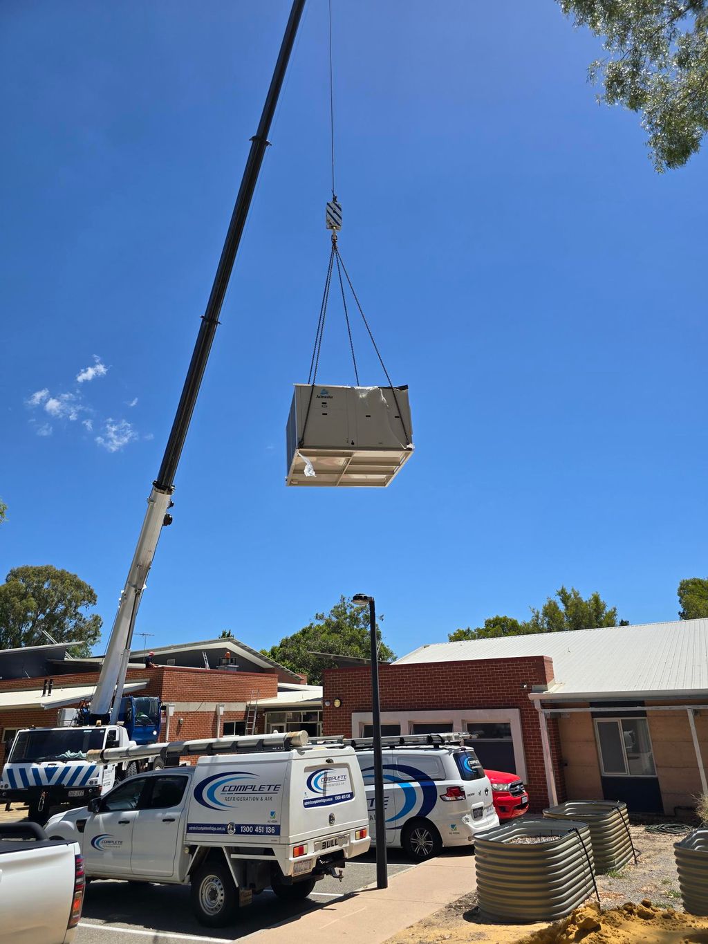 Crane lifting a large HVAC unit onto a brick building under a clear blue sky.