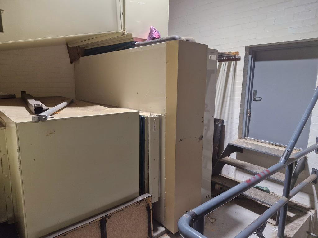 Side view of large indoor HVAC plant equipment beside access stairs and handrail.