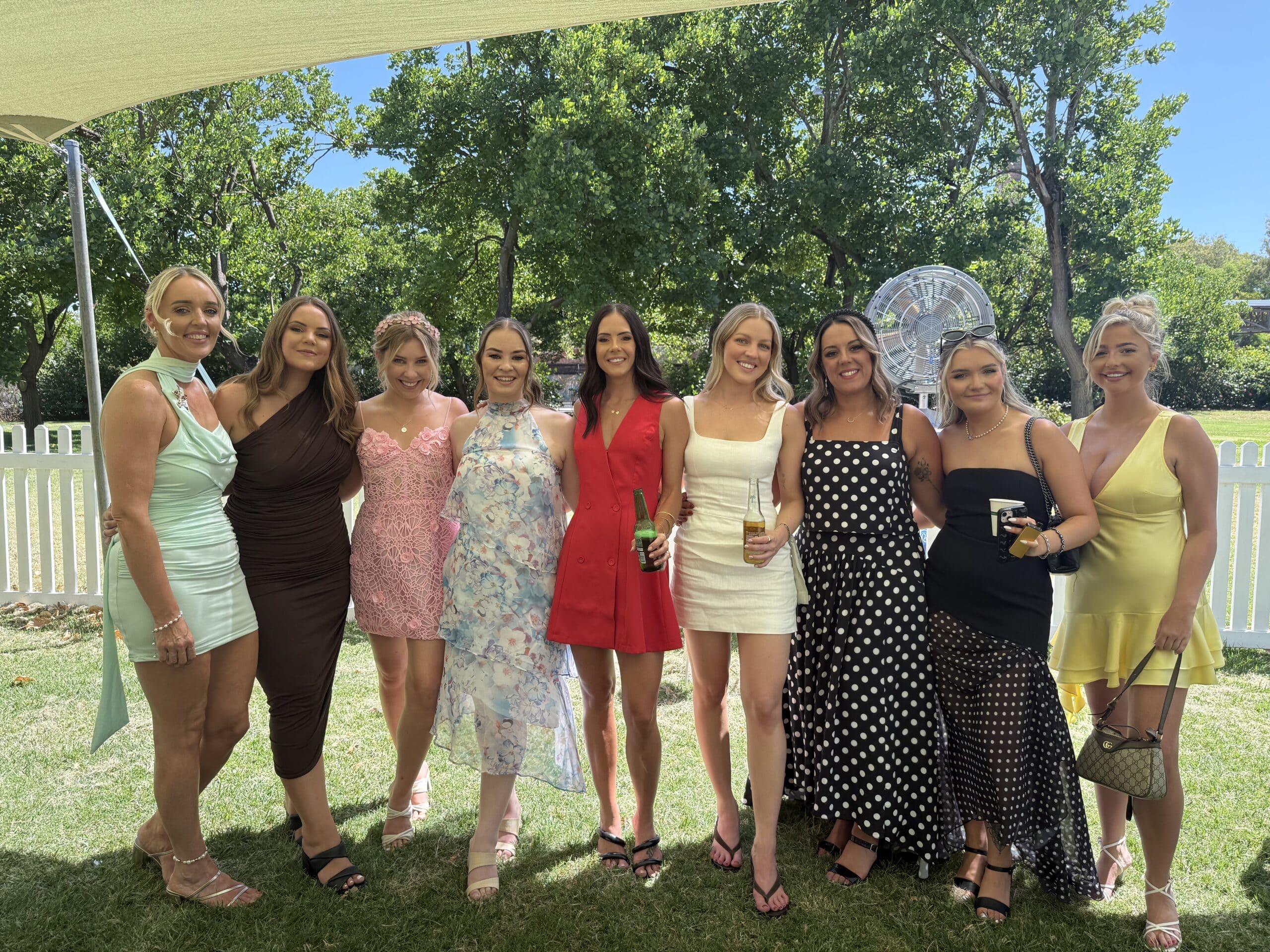 Group of women posing together in formal dresses at an outdoor garden celebration.