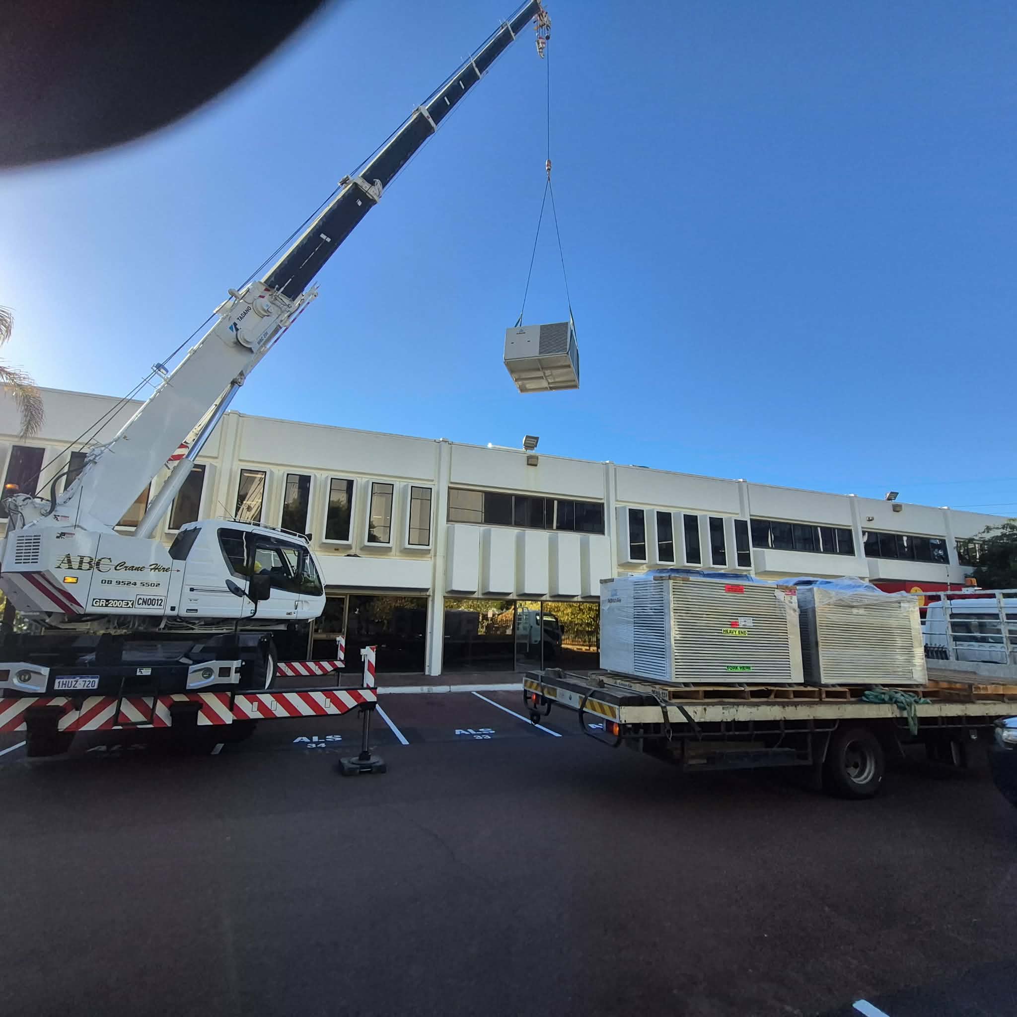 Crane installing a commercial rooftop HVAC unit from a delivery truck.
