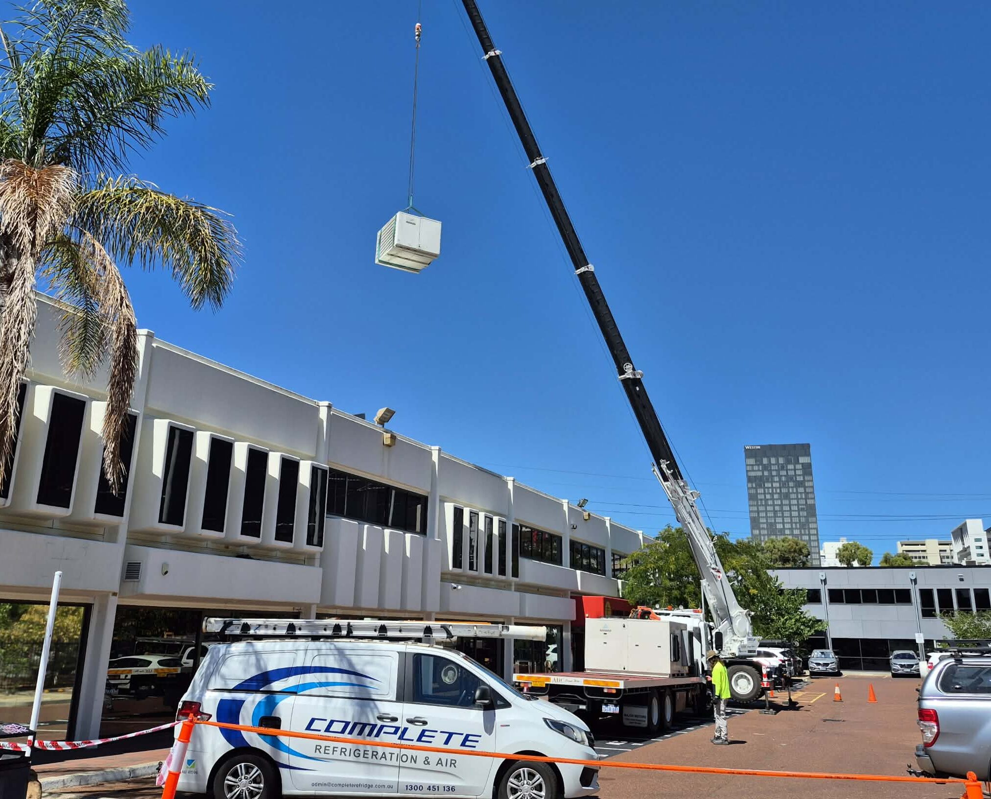 Crane lifting a rooftop HVAC unit into position for installation.