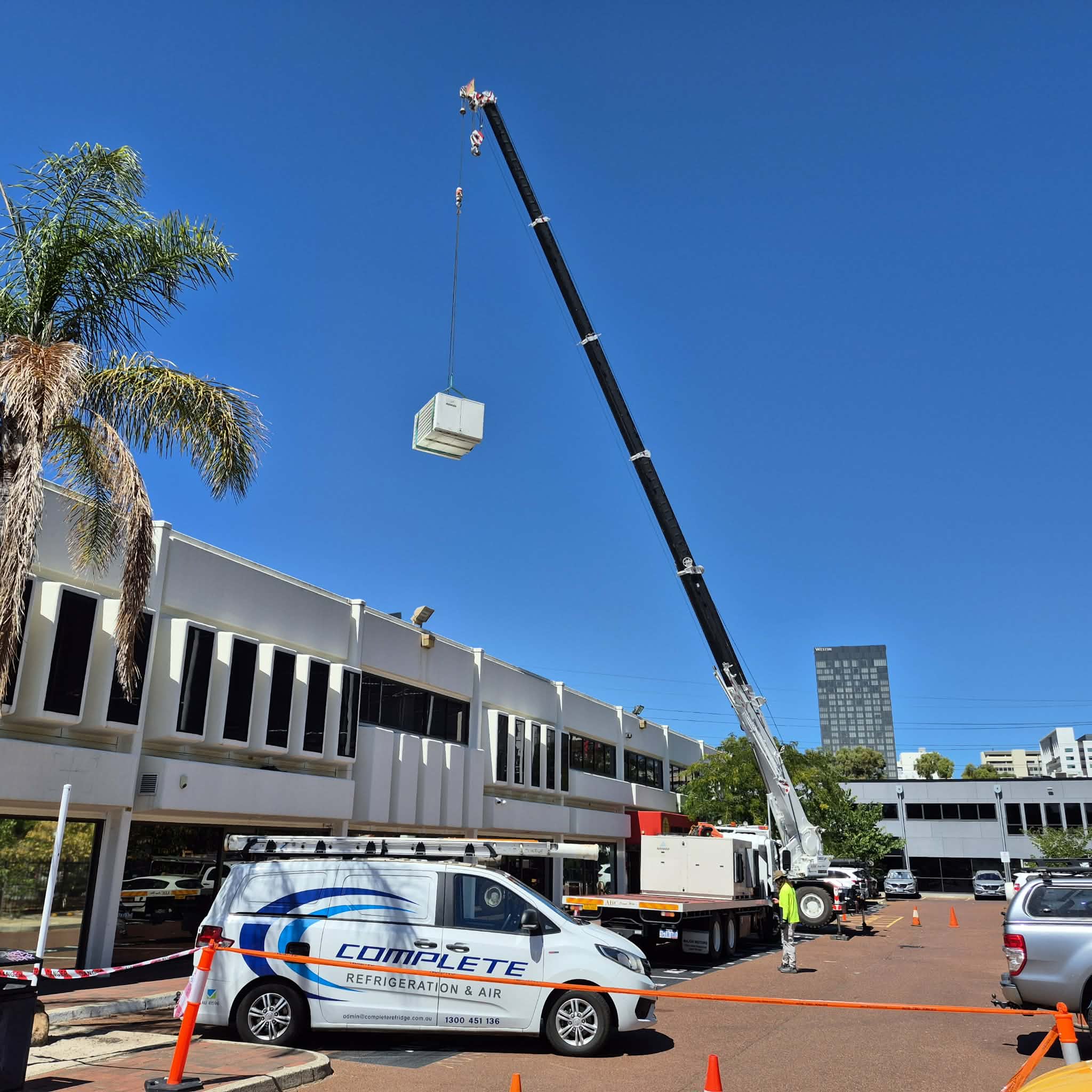 Crane lifting a rooftop HVAC unit into position for installation.