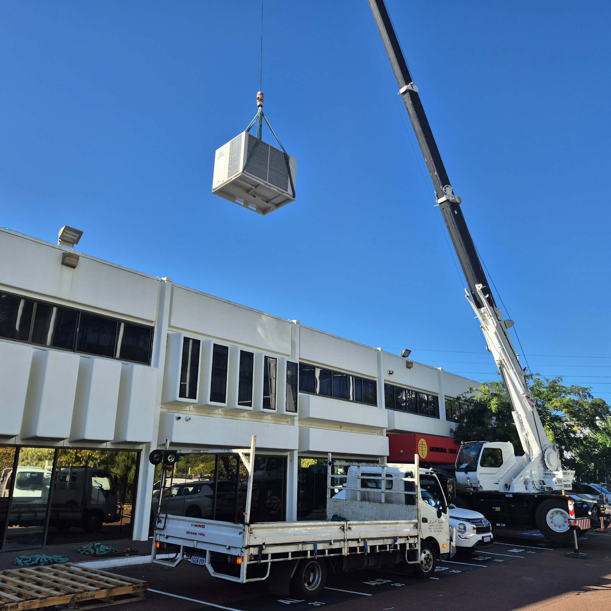 Commercial HVAC unit suspended by crane during rooftop installation.